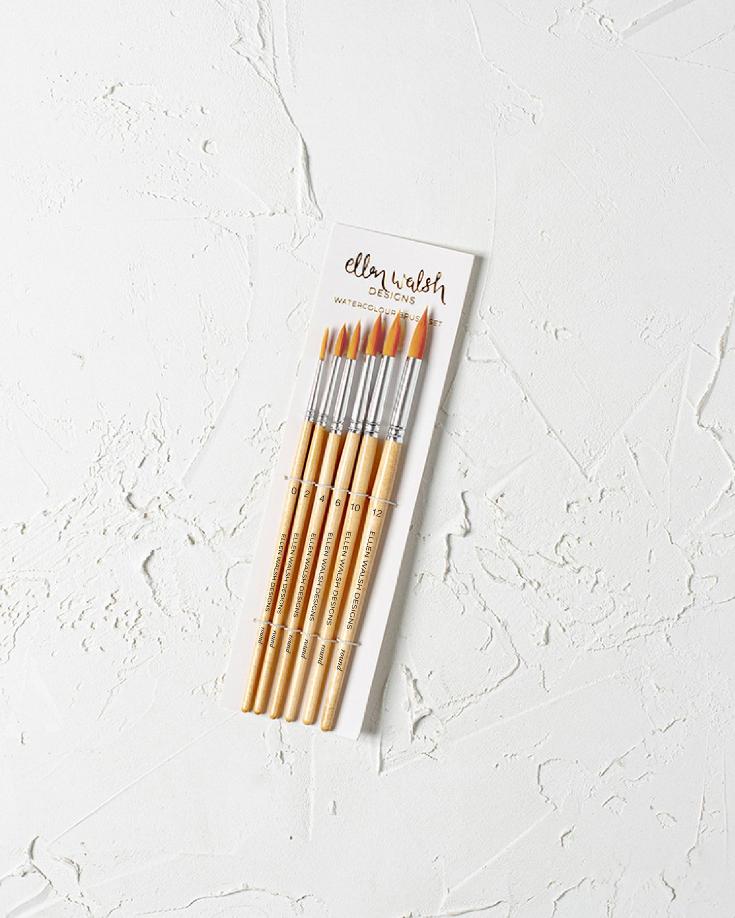 Set of watercolour paintbrushes in a cardboard holder on a textured white surface